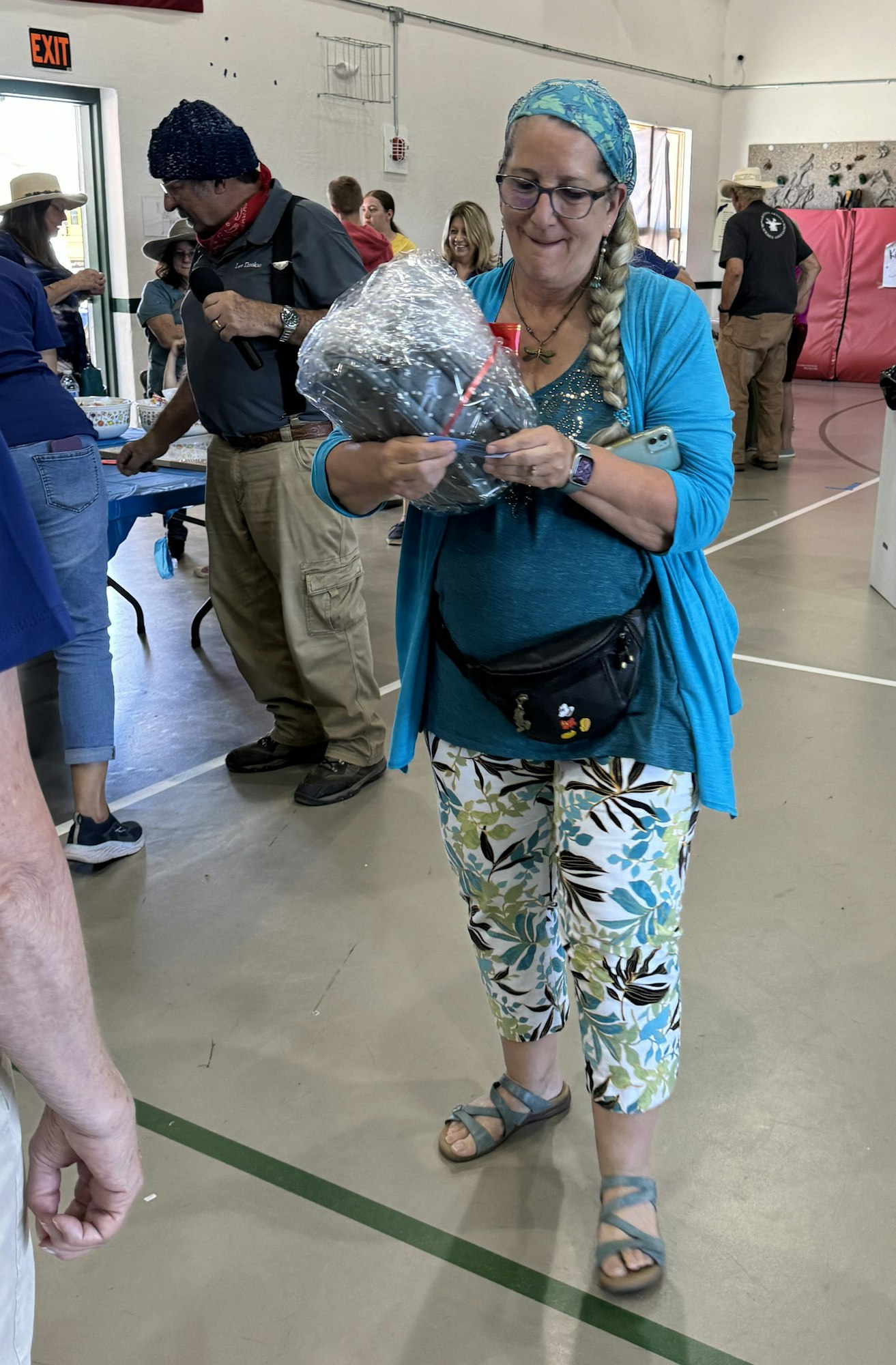 A smiling woman holding a wrapped item in a crowded indoor space.