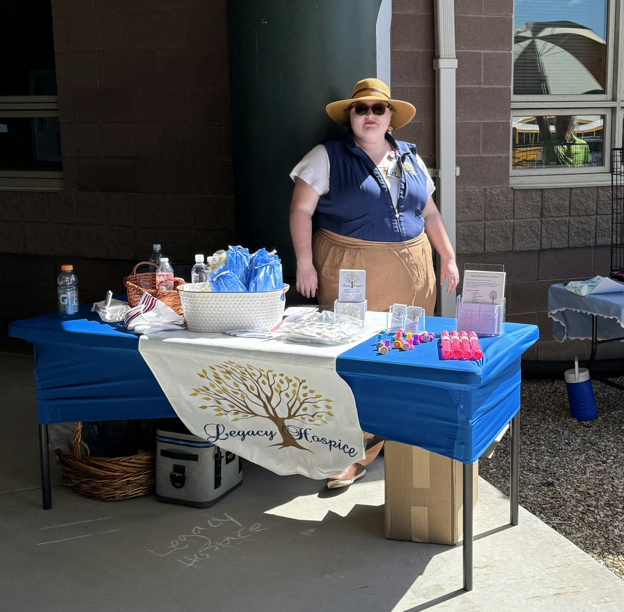 A person stands behind a table with information and promotional items under a "Legacy Hospice" banner.