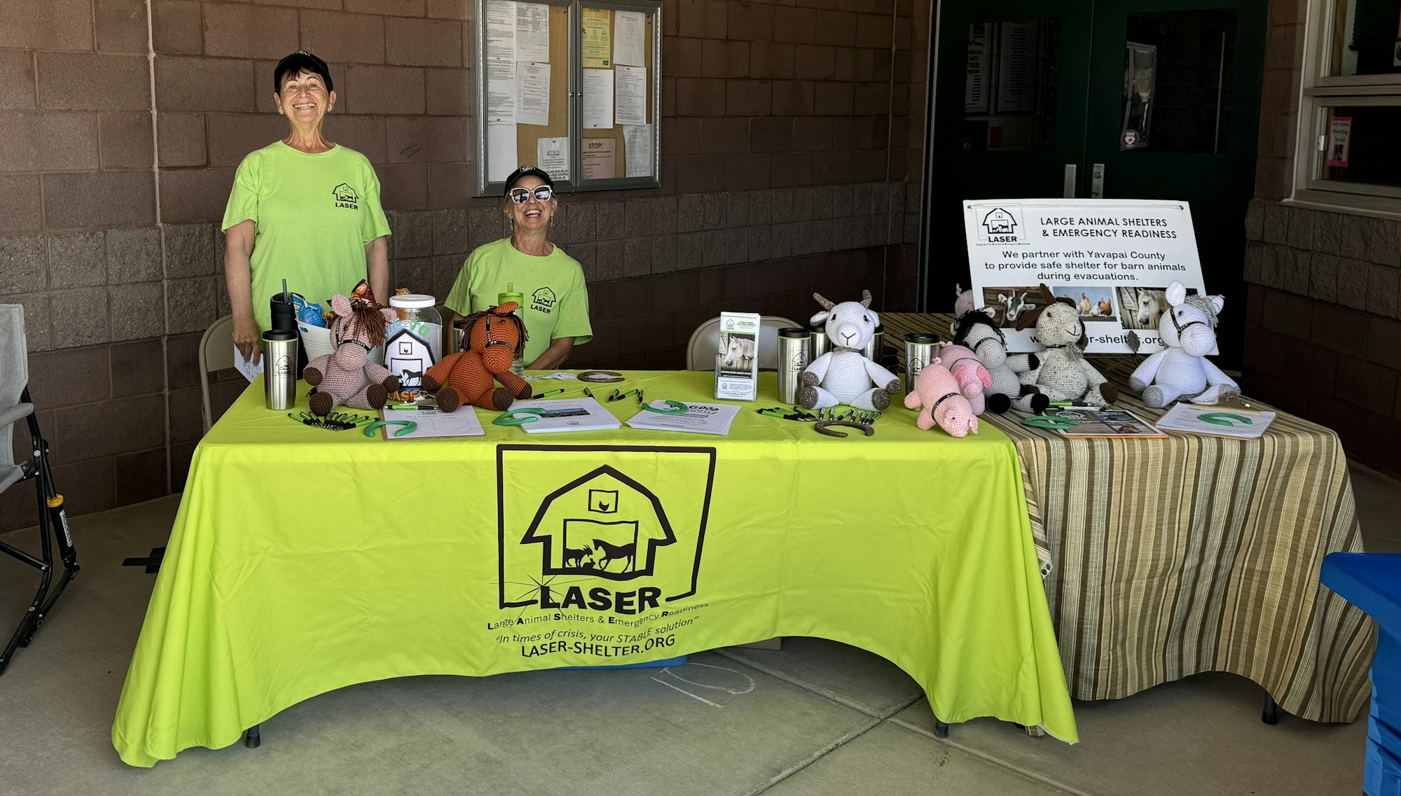 Two people at a booth with stuffed animals and information about emergency animal shelter services.