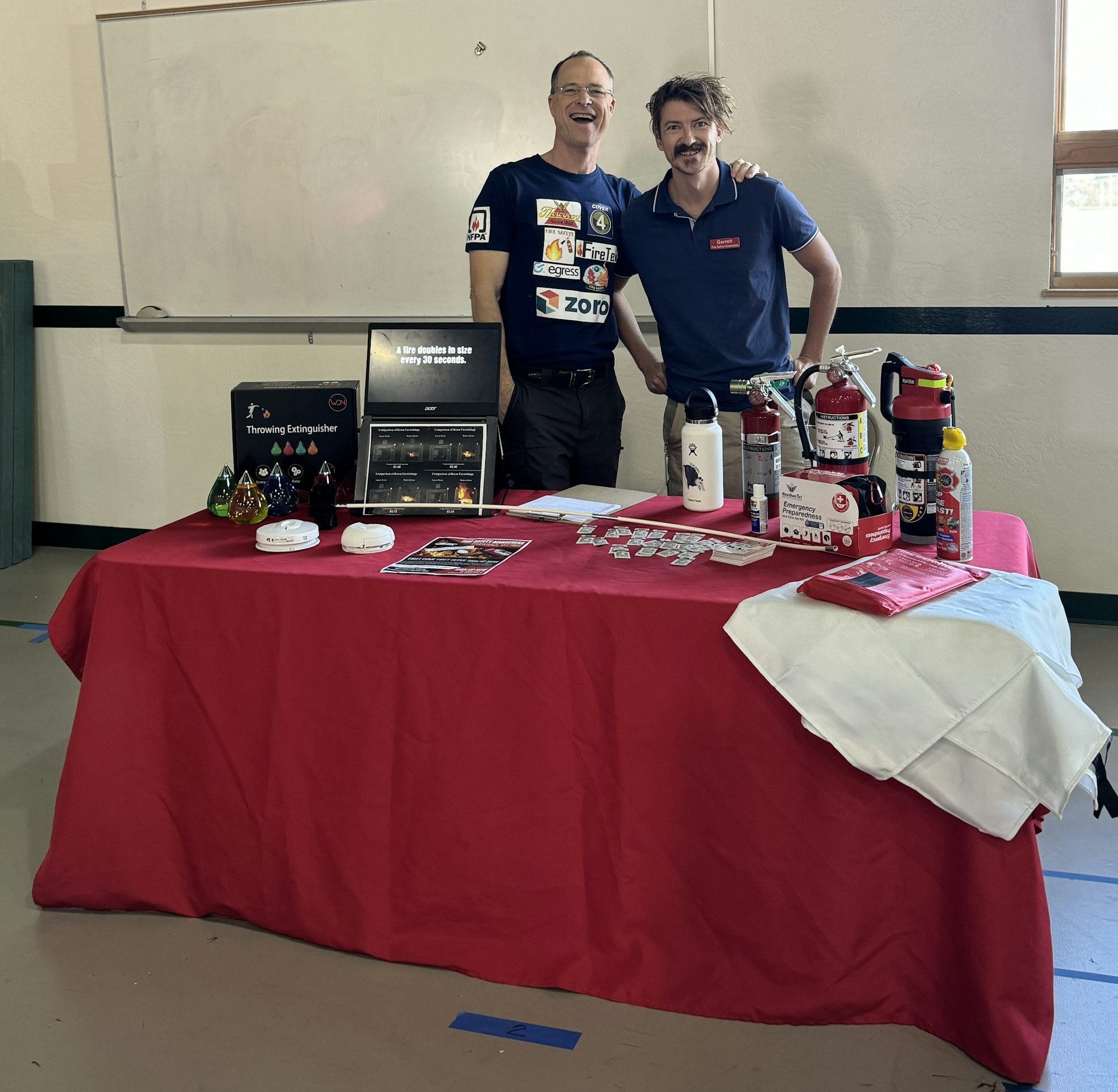 Two individuals standing behind a table displaying fire extinguishers and promotional materials.