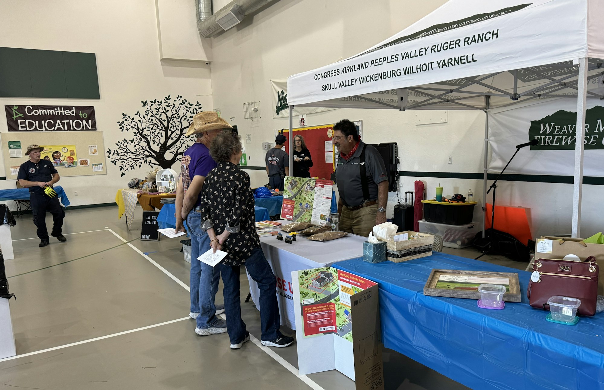 An indoor event with informational booths, people interacting, a firefighter, and educational materials on display.