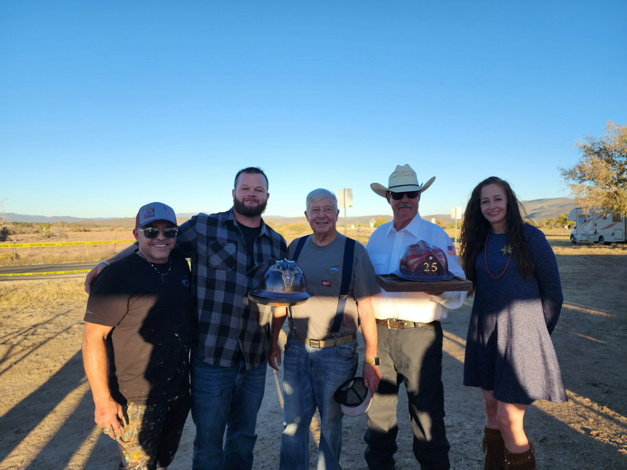 Five people outdoors, two holding firefighter helmets.