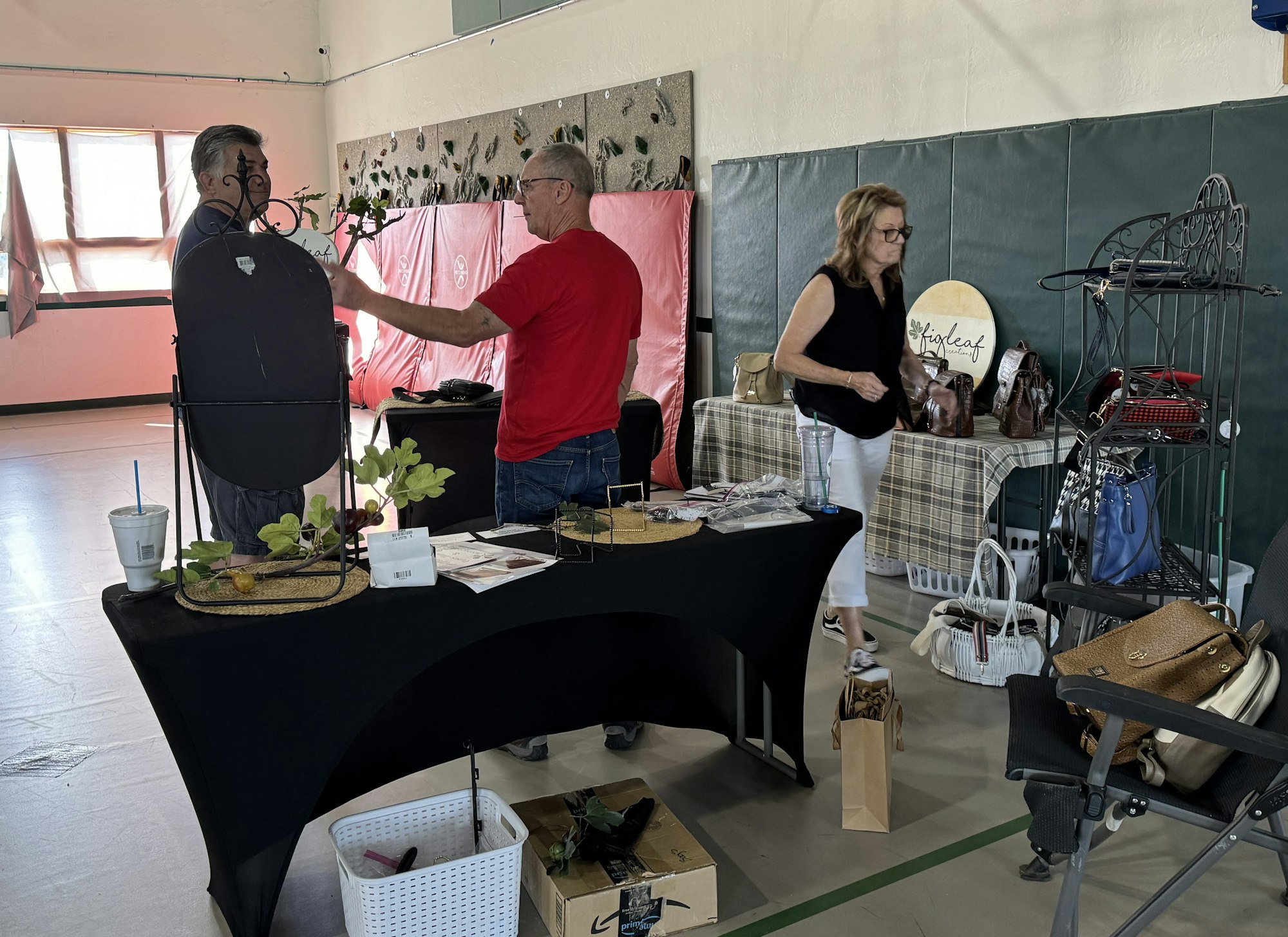 An indoor market scene with people at a stall displaying products, including handbags and small home decor items.