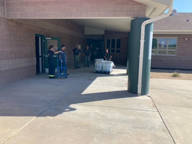 People with a hand truck and a pallet of goods outside a building.