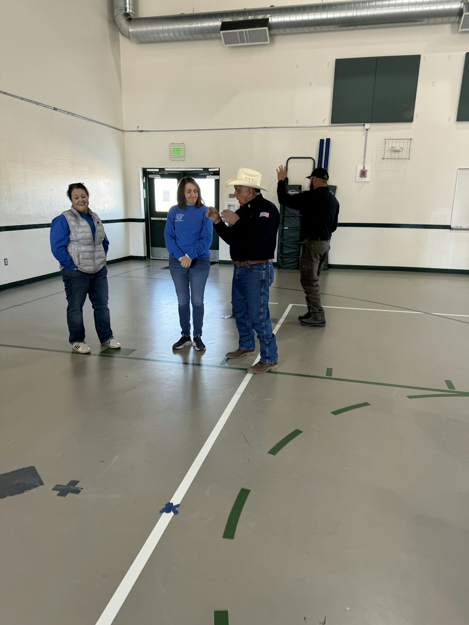 Four people standing in a gymnasium; one wears a cowboy hat.