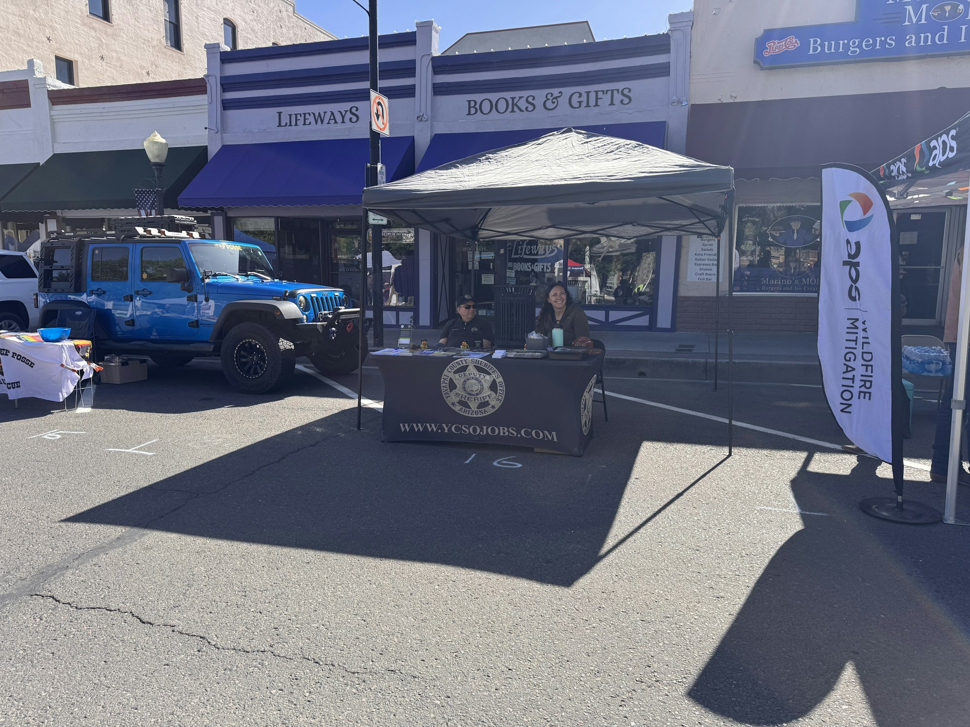A blue Jeep parked beside a booth with a table, where two people are promoting jobs and wildfire mitigation.