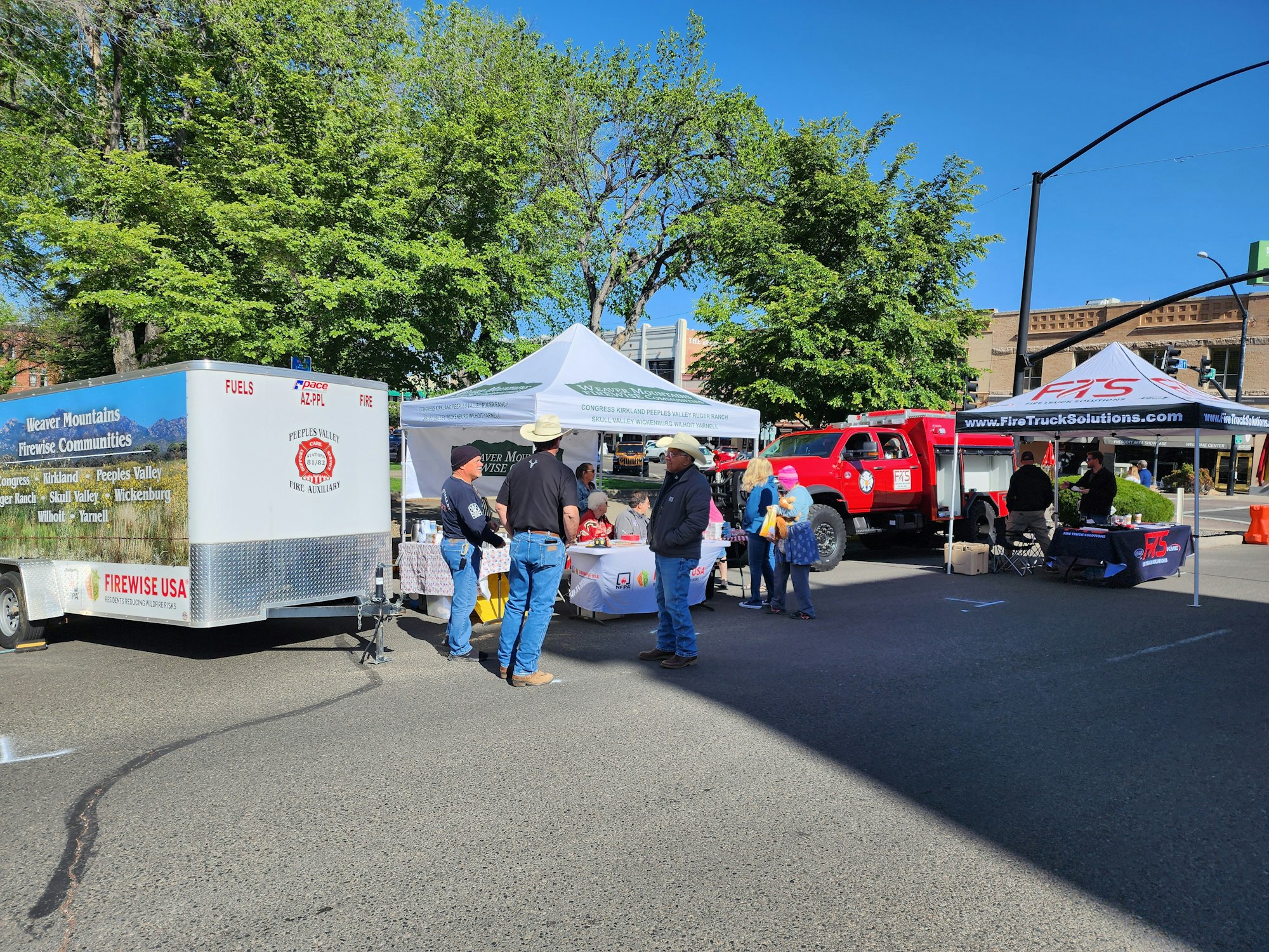 A community event with tents, a fire truck, and people engaged with fire safety displays and discussions.