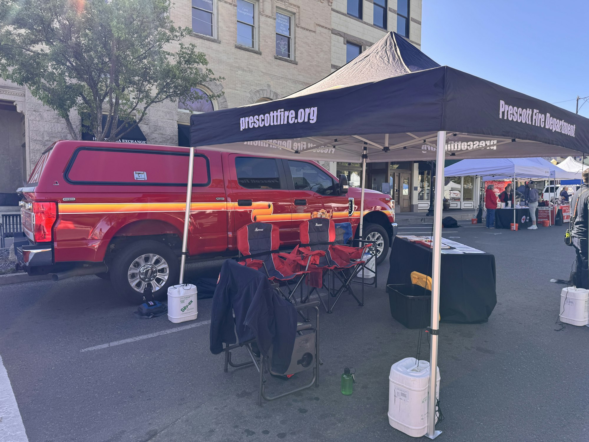 A Prescott Fire Department tent with a red truck parked nearby and some folding chairs set up at a market or event.