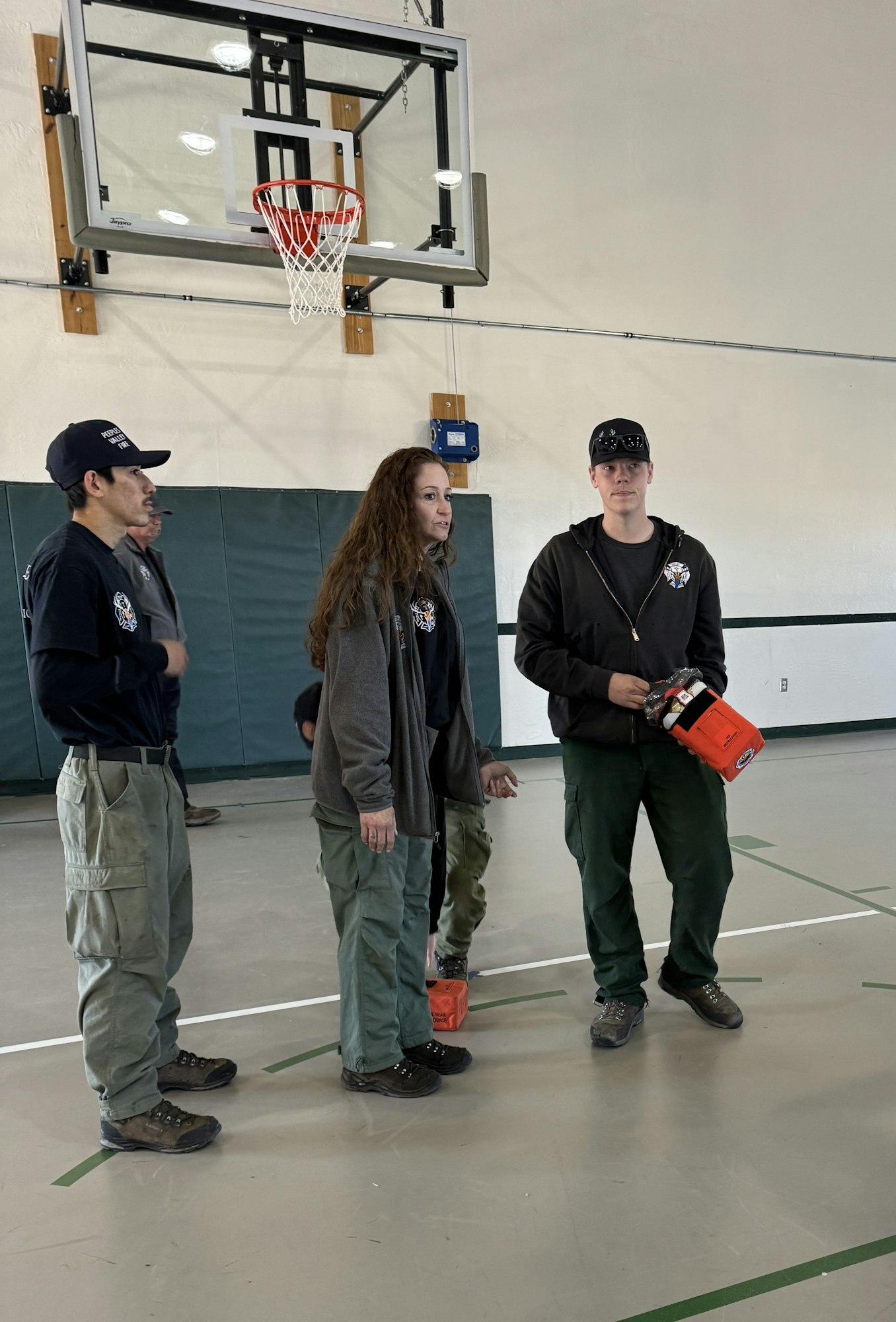 People in uniform standing in a gymnasium under a basketball hoop, holding an orange object.