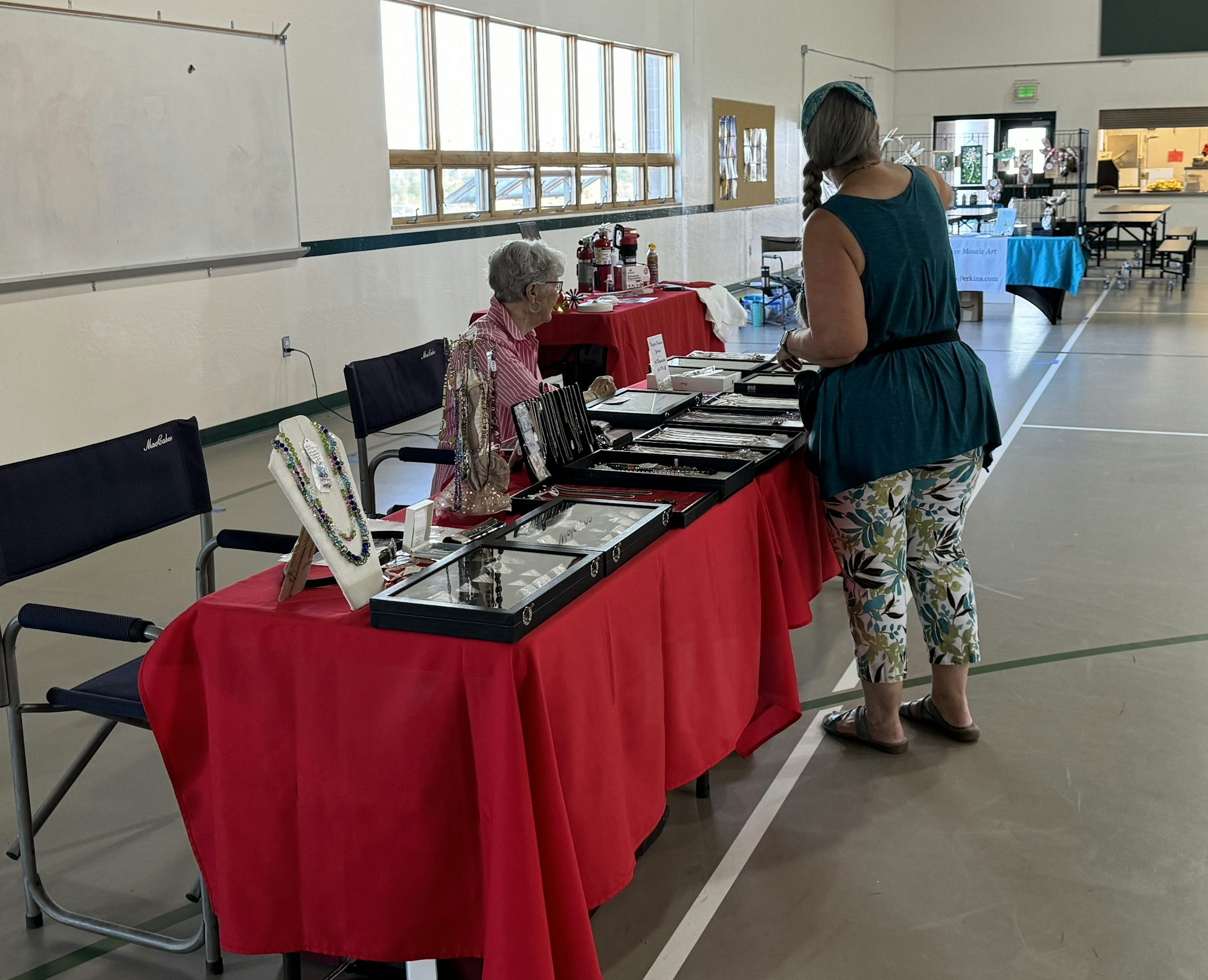 Indoor craft fair with jewelry on display and two women, one browsing the items.