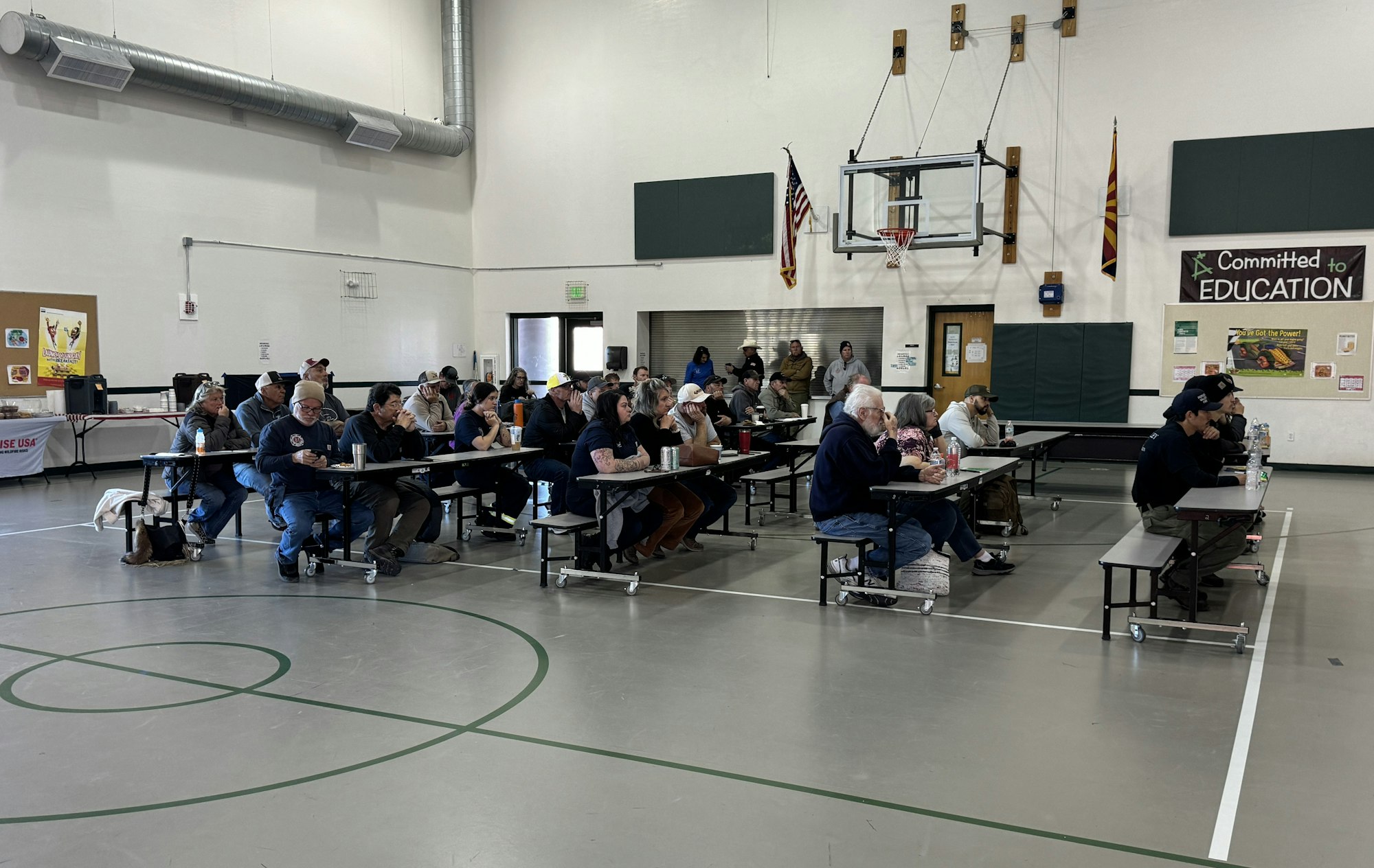A group of people seated at tables in a gymnasium, attending an indoor event.