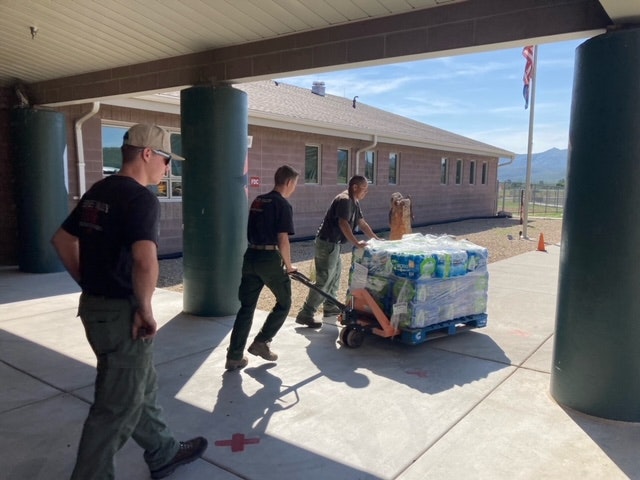 Three people transporting supplies on a dolly with an American flag in the background.