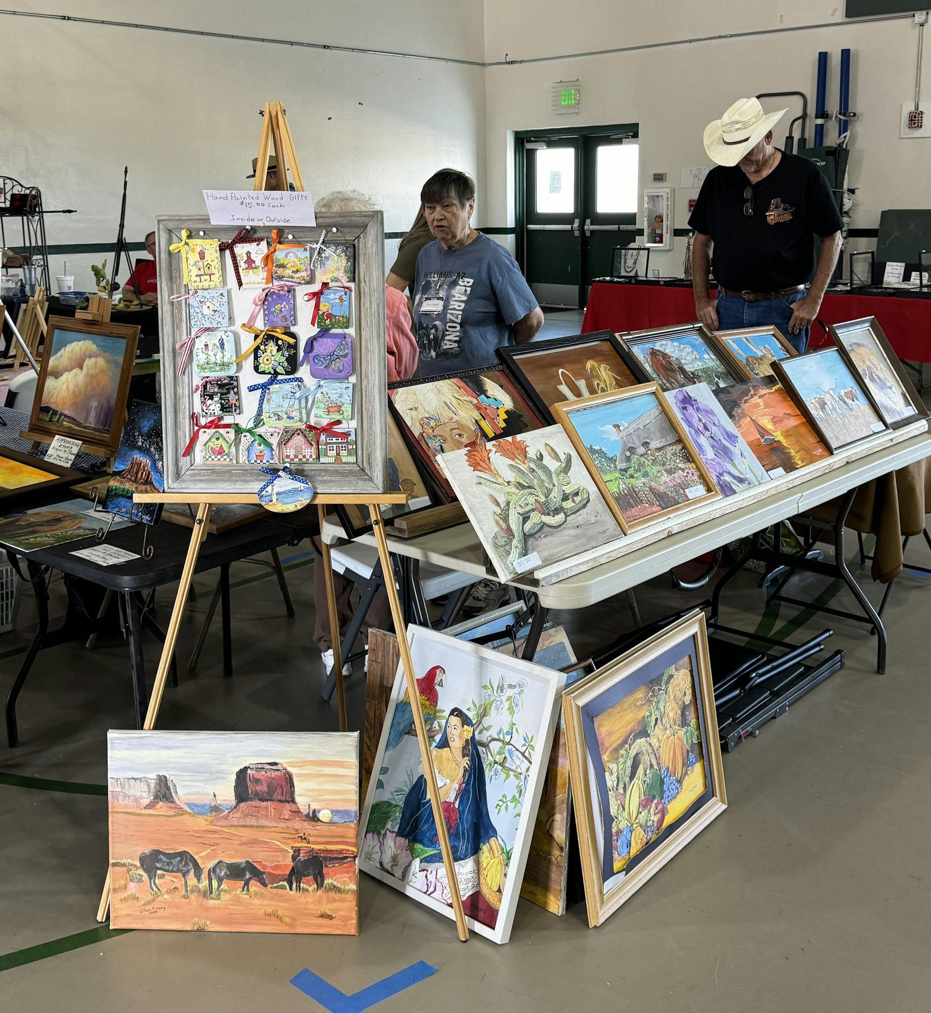 An art display with various paintings and two people browsing in an indoor setting.
