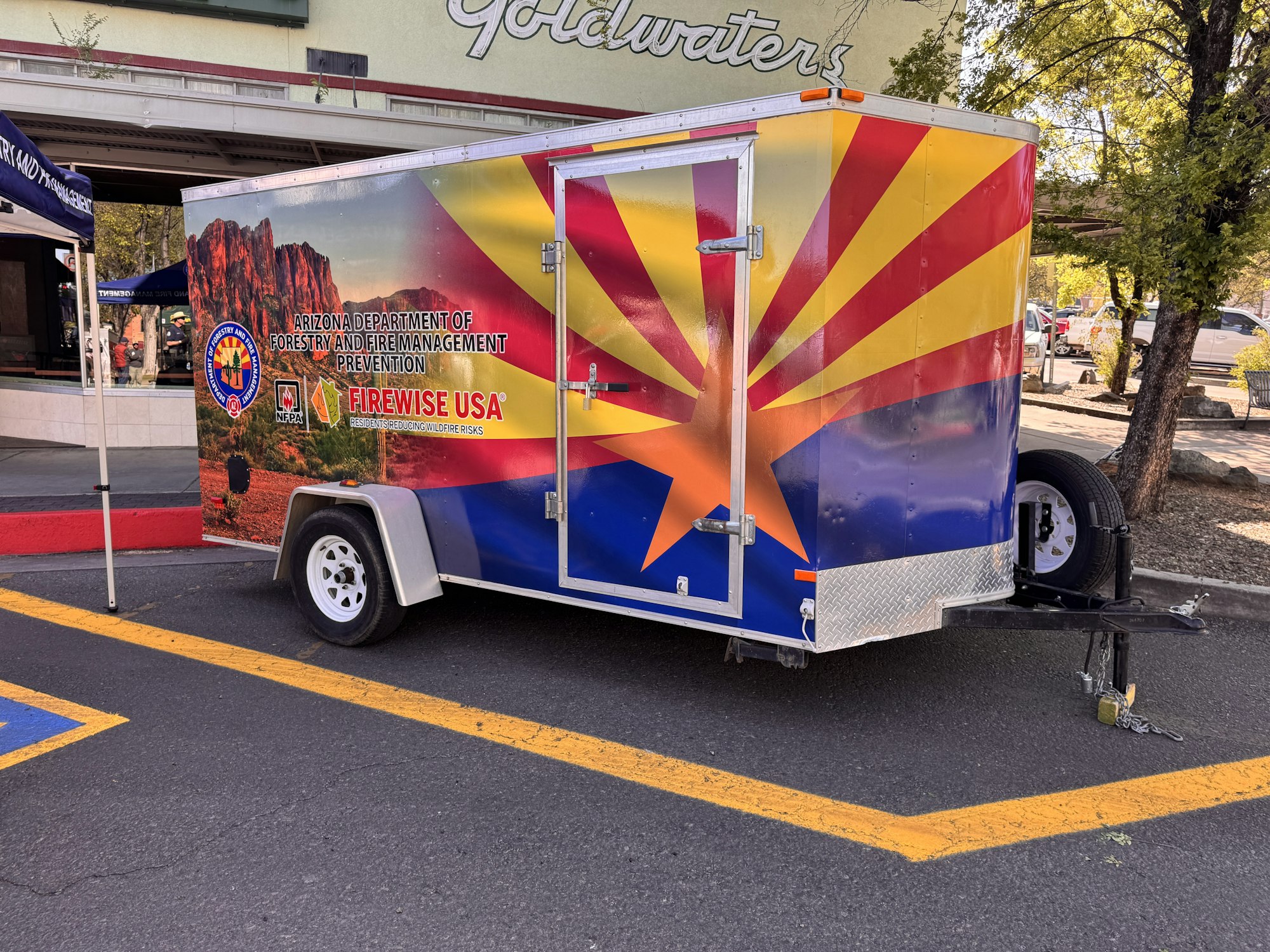 The image shows a colorful trailer representing the Arizona Department of Forestry and Fire Management, promoting wildfire prevention.