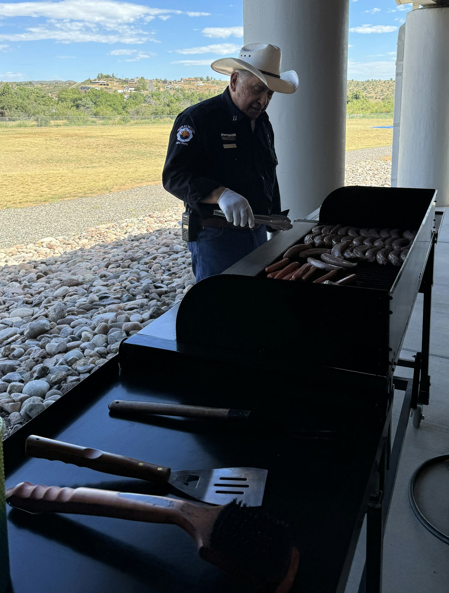A person in a cowboy hat grilling sausages and hot dogs.