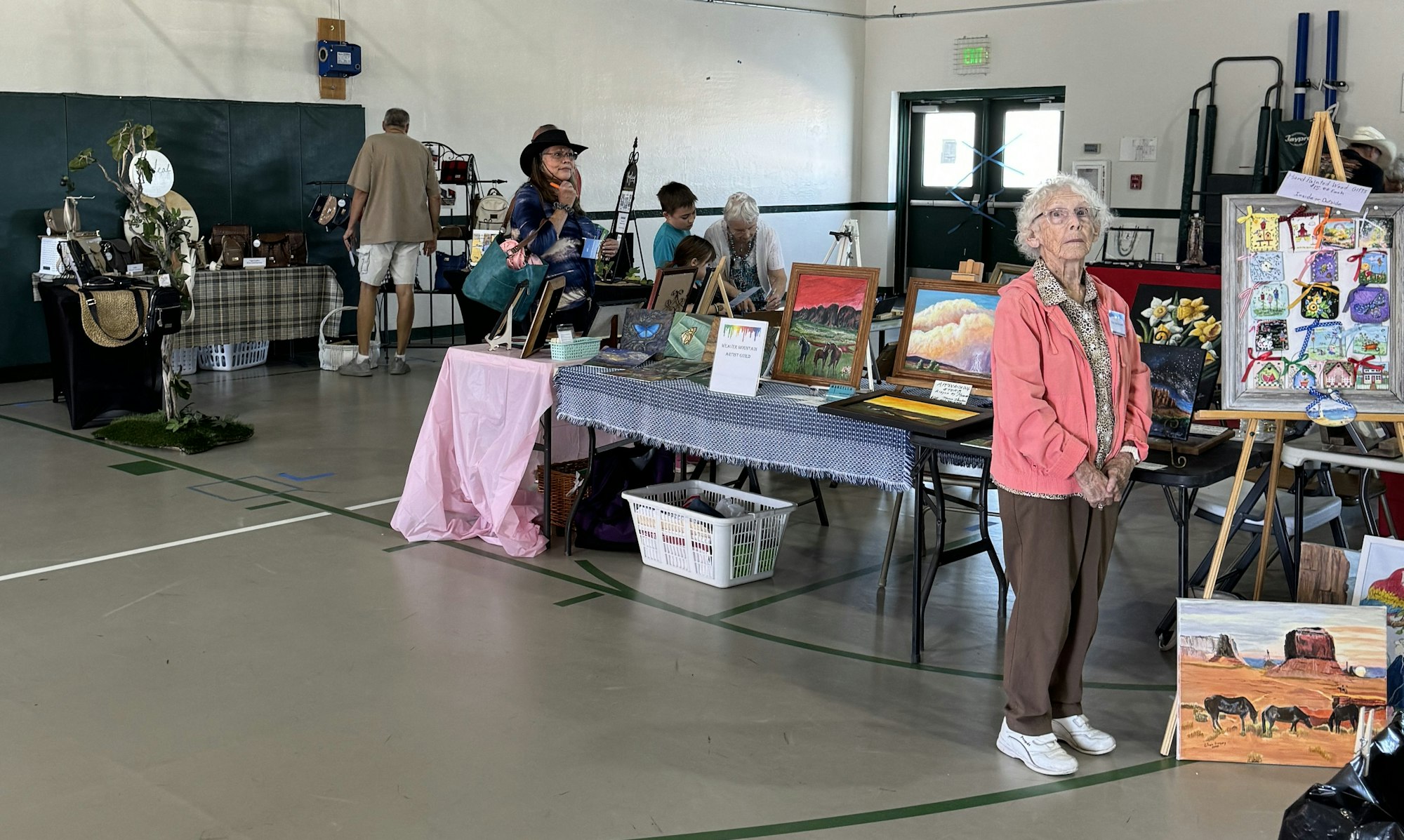 An indoor craft fair with people, artwork, and handmade items on display.