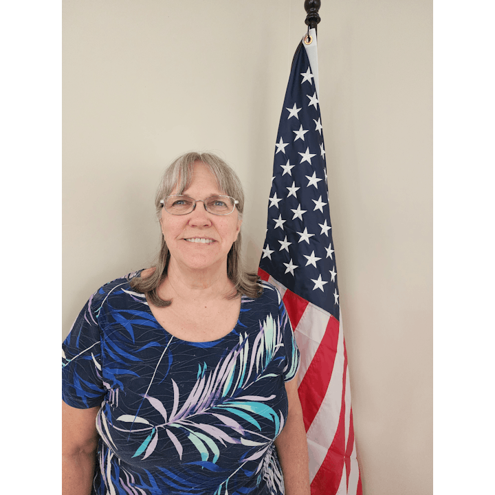 A person smiling in front of an American flag.