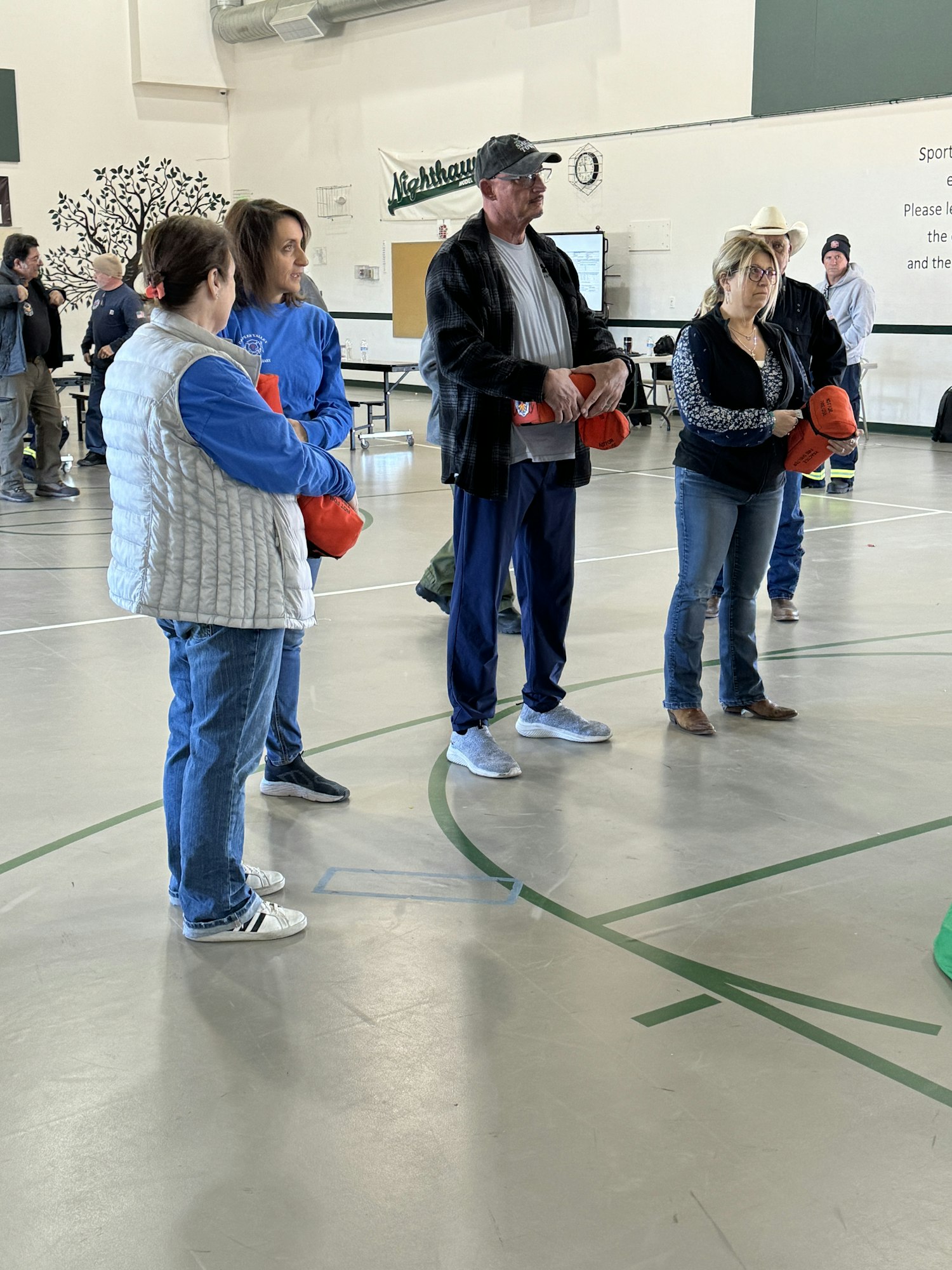 People standing in a gym, holding orange bags, possibly in a group activity or event.