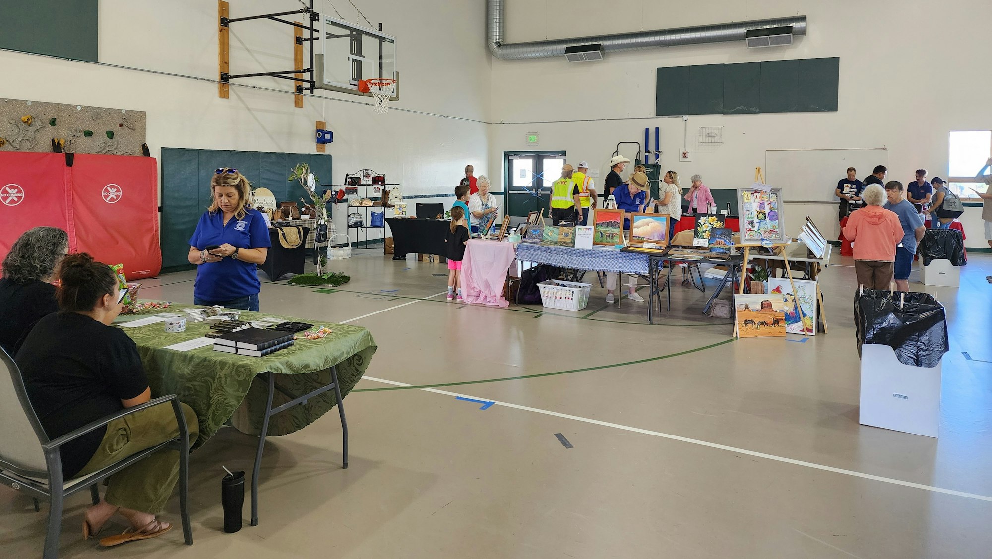An indoor craft fair with vendors, artwork displays, and visitors in a gymnasium.