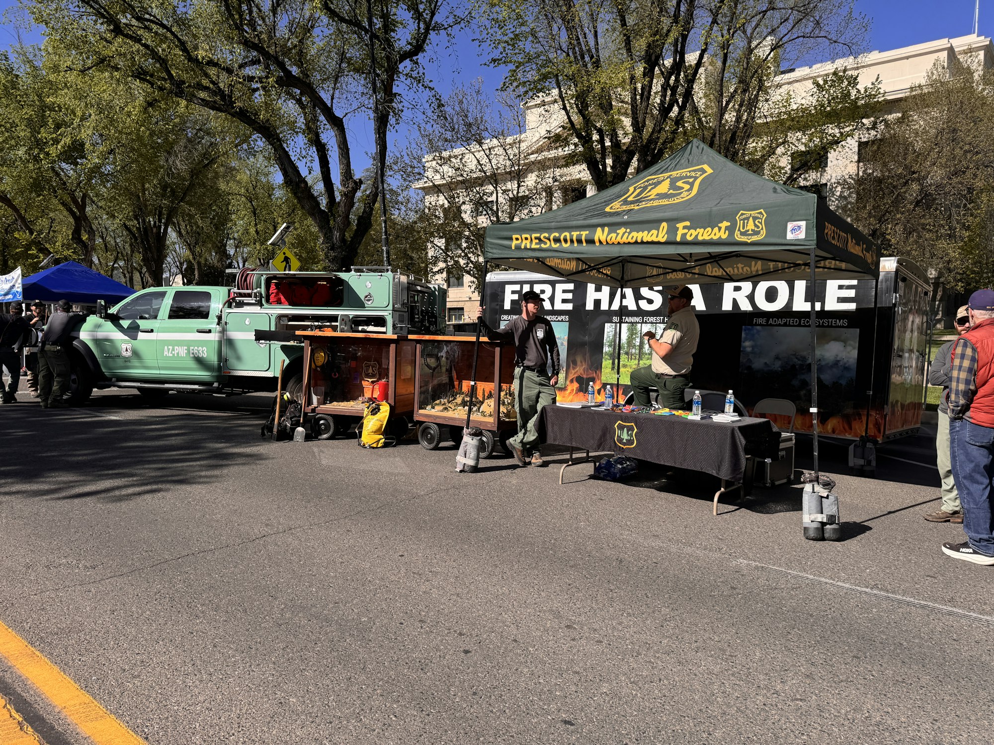 A Prescott National Forest booth displays fire education, with a green truck and visitors engaging in activities.