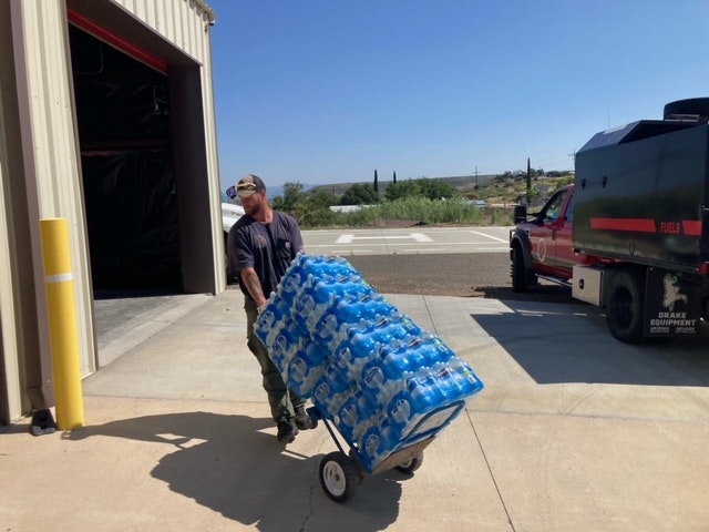 A man pushing a dolly loaded with water bottle packs outside a building.