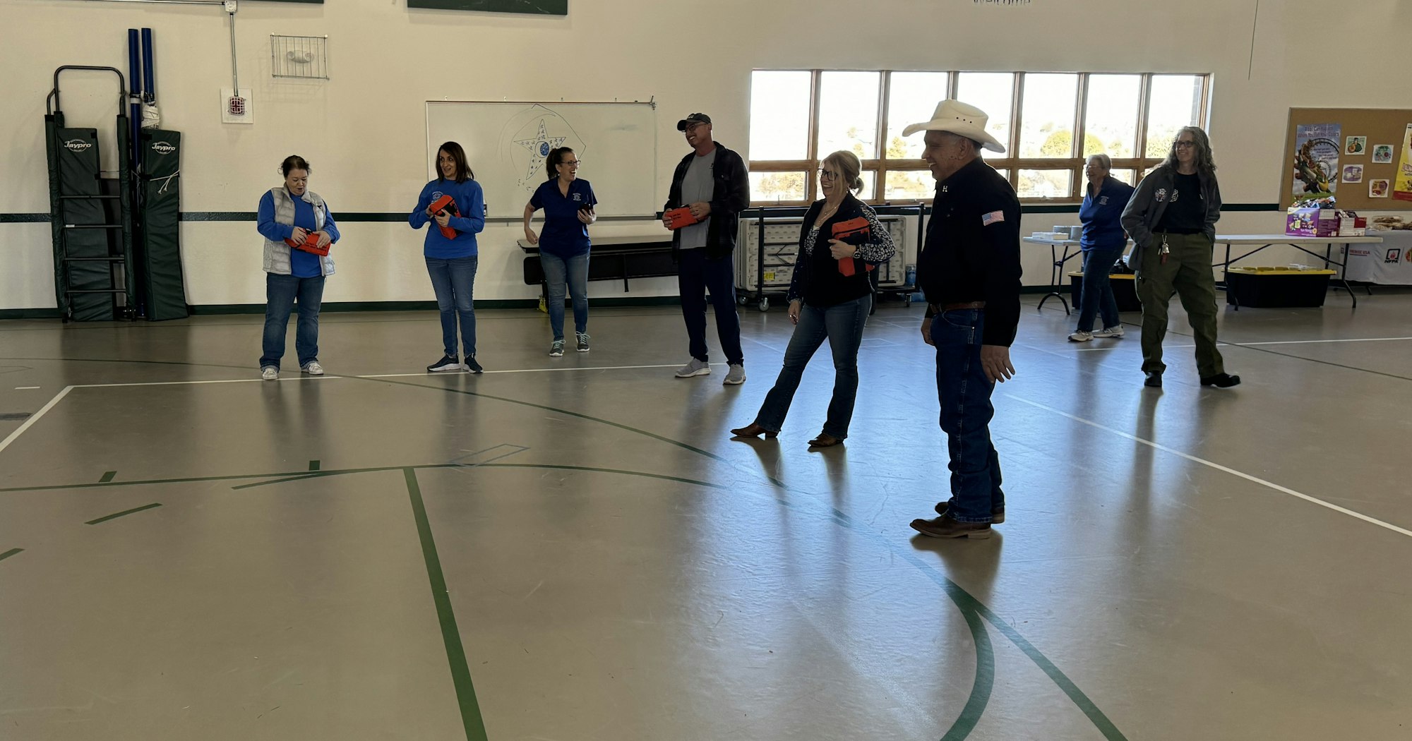 A group of people in casual clothing holding red objects, standing indoors on a sports court.