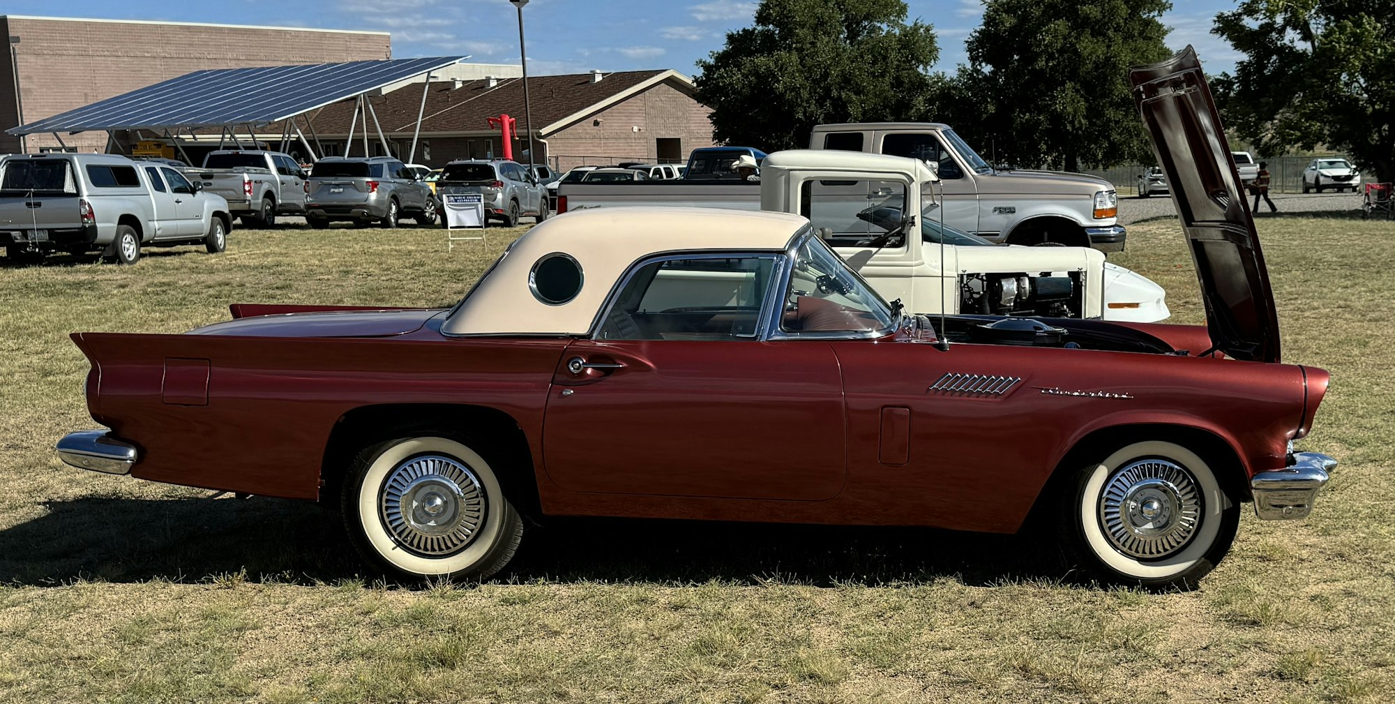 A classic red car with a white soft top at a vehicle show, hood open, displaying its engine.