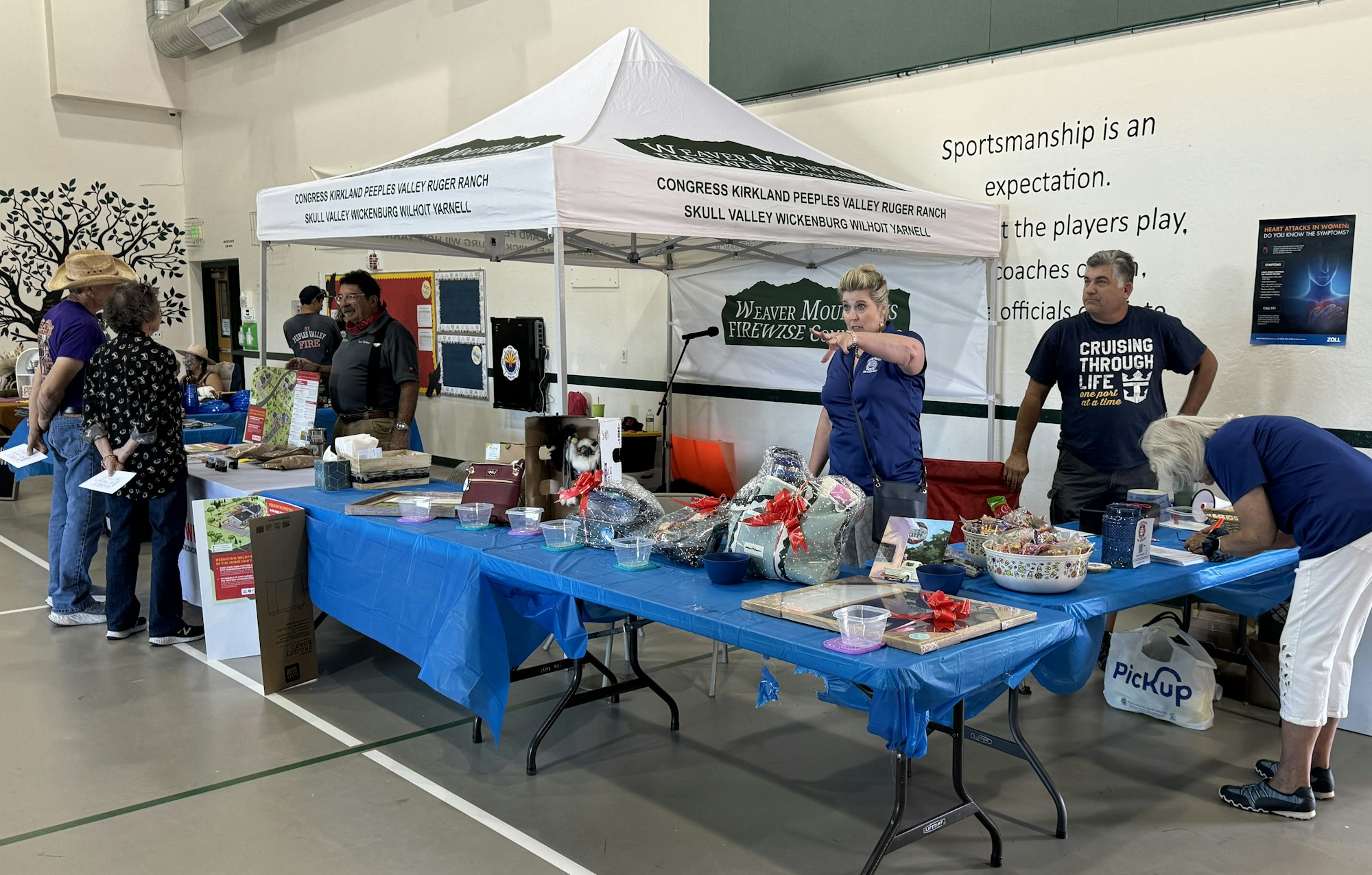 An indoor event with people at booths, displaying various items on tables, under signs for a firewise community.