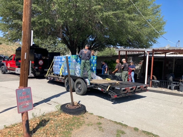 People unloading water bottle packs from a trailer. Sign says "NO PARKING FIRE LANE".