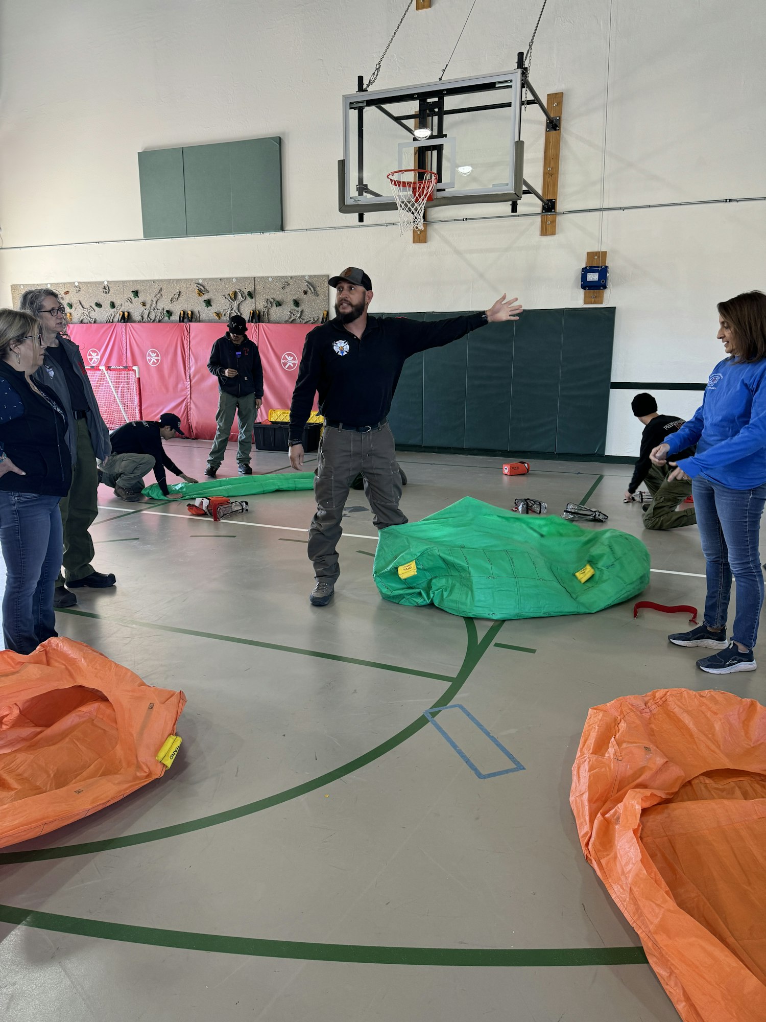 People in a gym with colored tarps on the floor and a basketball hoop in the background.