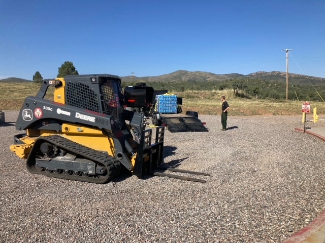 A skid-steer loader, pallets on a trailer, and a person in an outdoor setting.