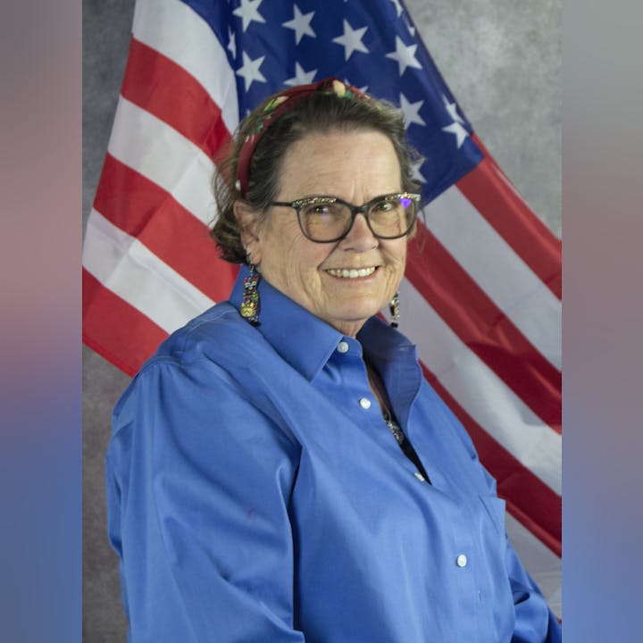 A smiling woman with glasses in front of an American flag.