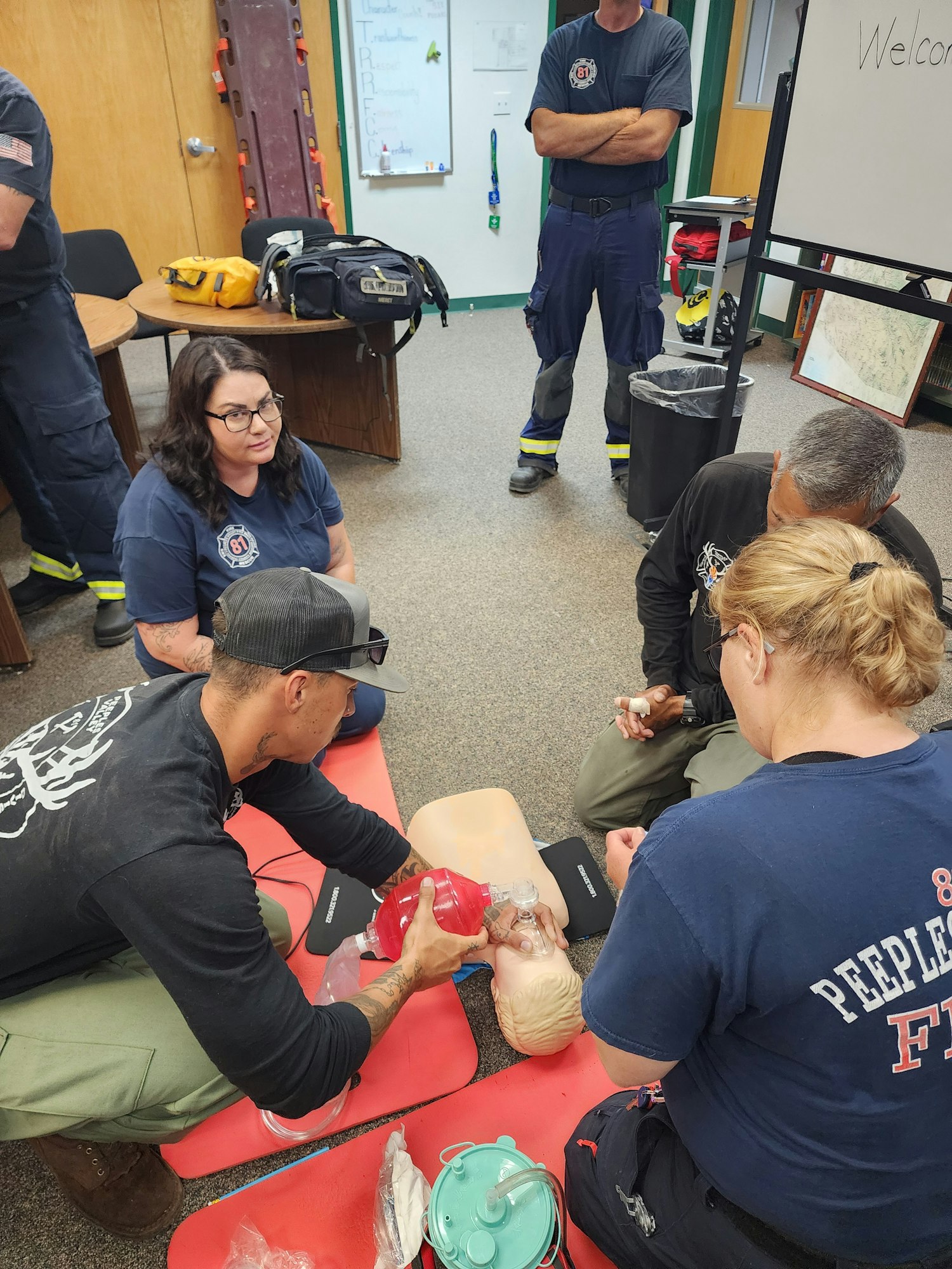 Firefighters are practicing CPR and using a training mannequin in a classroom setting.