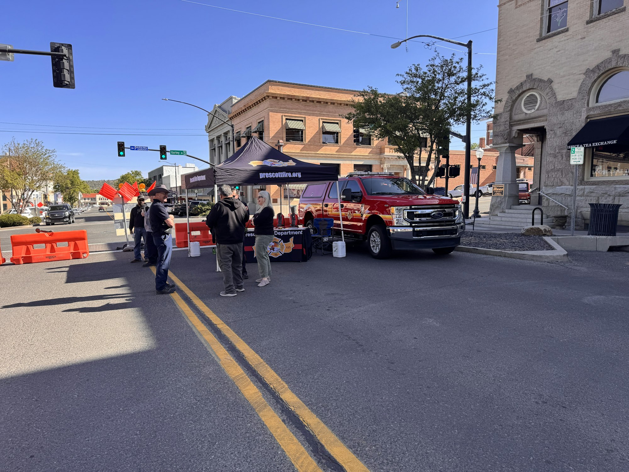 A street event with a red truck, a tent, and people gathered near barriers, indicating an informational or community activity.