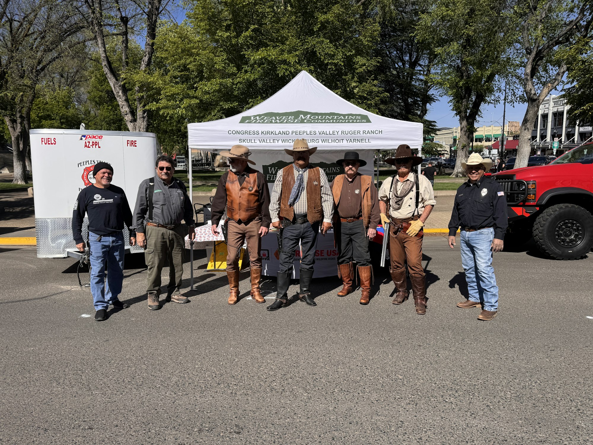 A group of individuals dressed in western attire stands in front of a tent, promoting a ranch at an outdoor event.