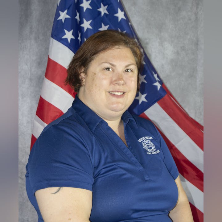 A woman in a blue uniform with an American flag in the background.