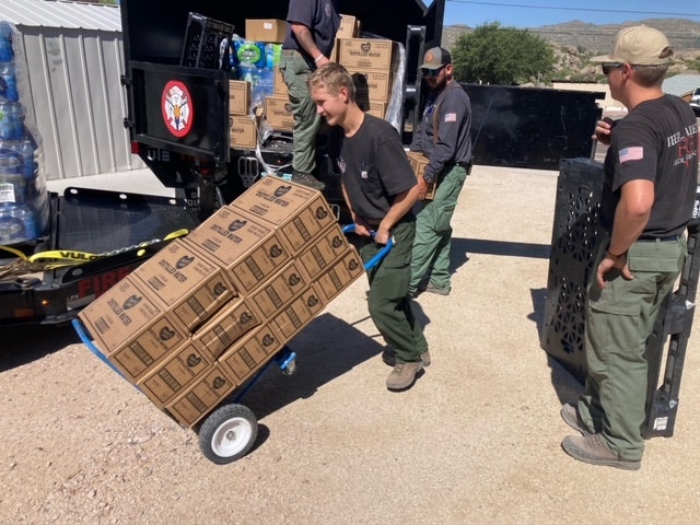 People unloading supplies from a truck, using a hand trolley.