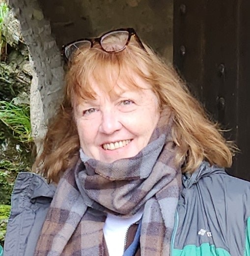 A smiling woman with a scarf and sunglasses on her head, outdoors.