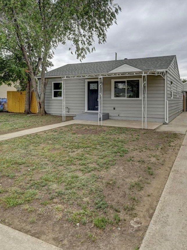 Before installation of a residential raingarden; small gray house with a front porch, tree on the side, and a patchy grass yard.