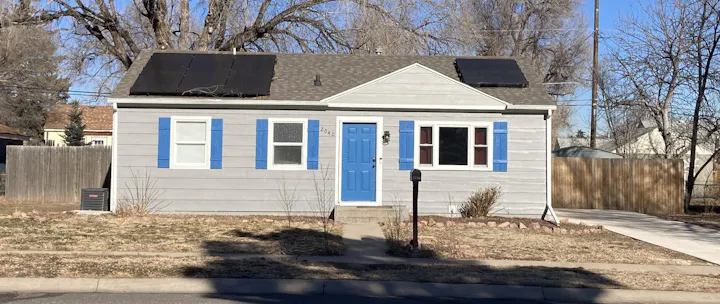 A light gray house with blue shutters and door, featuring solar panels on the roof and a concrete walkway. Typical residential front yard in Stratton Meadows before raingarden installed.