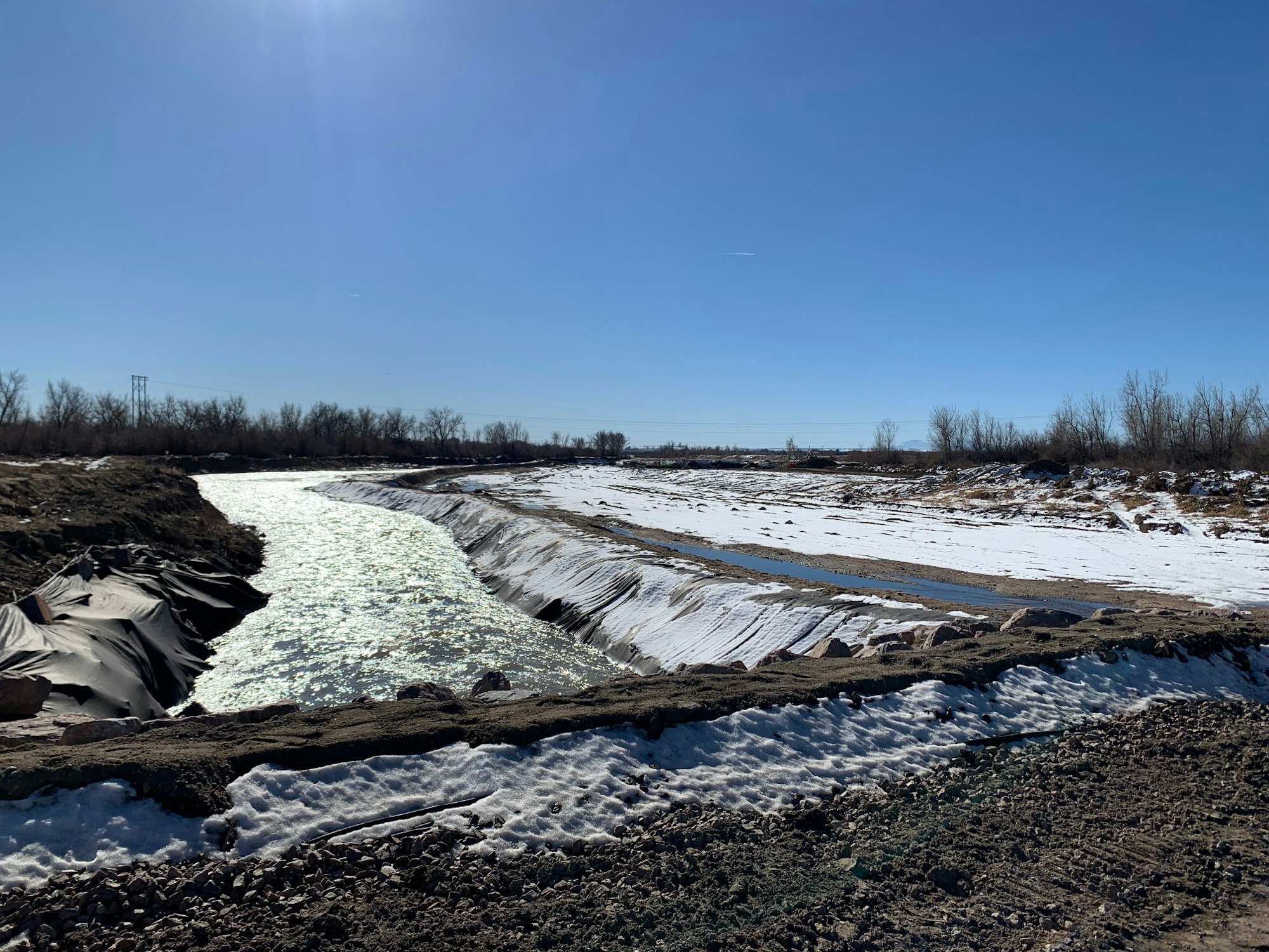 A river with surrounding snow-covered banks under a clear blue sky.