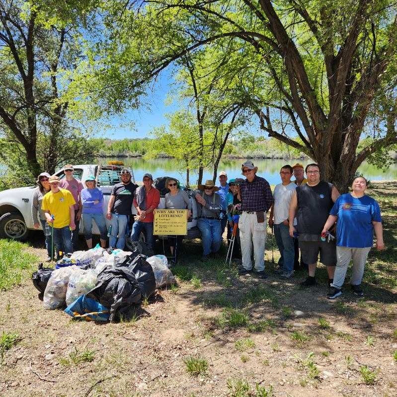 A group of people posing with collected trash bags near a lake, with a sign about littering.
