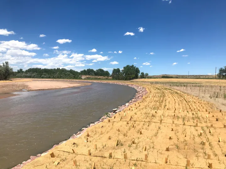 A river curves through a landscape of sandy banks and green vegetation under a blue sky with scattered clouds.