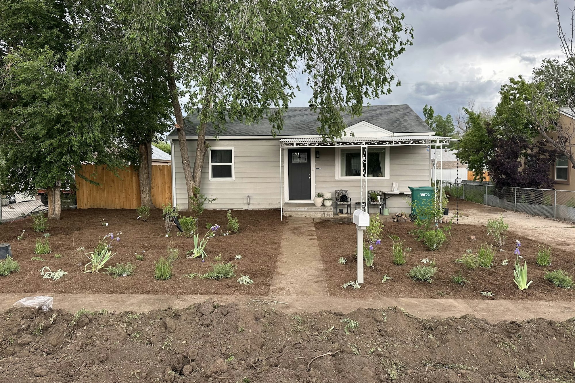 After installation of a residential raingarden; small house with a freshly landscaped yard, featuring new plants, mulch, and a pathway leading to the entrance.