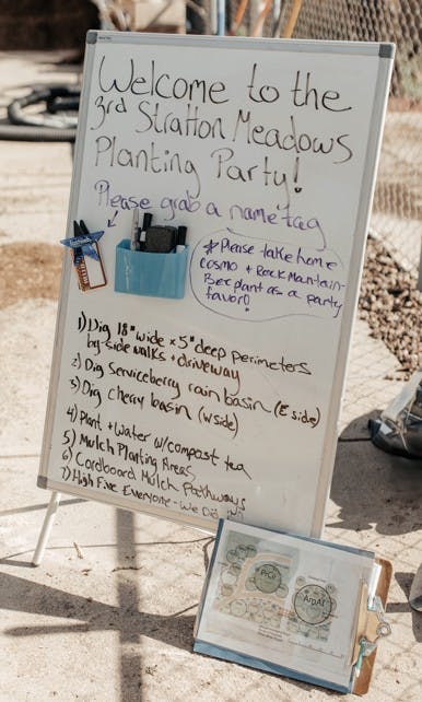 A whiteboard at the "3rd Station Meadows Planting Party" with tasks for digging, planting, and mulching, plus name tags and party favors.