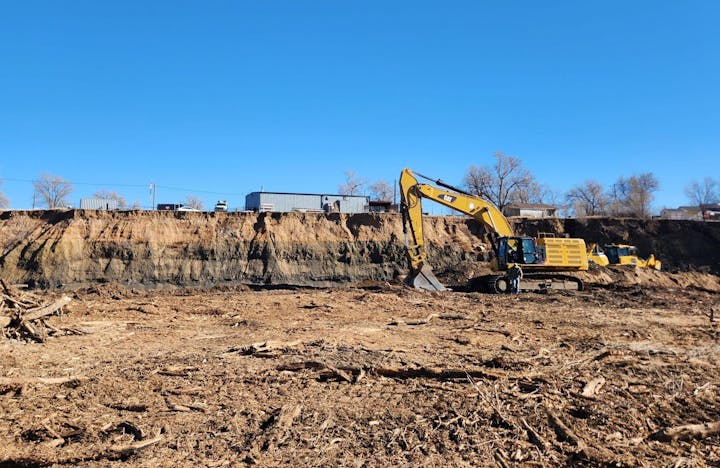 Construction site with excavators clearing land under clear blue sky.
