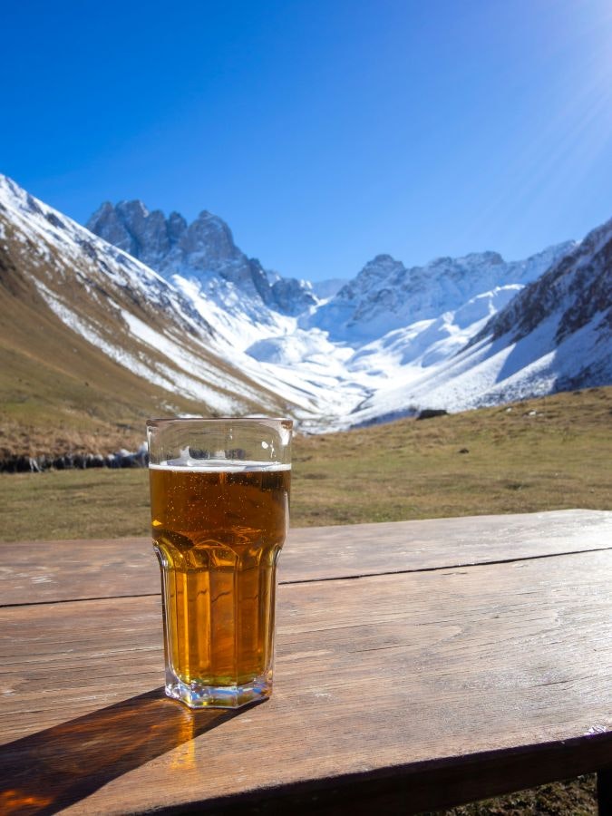 A pint of beer on a wooden table with a snowy mountain landscape in the background. Photo by Yoav Aziza on Unsplash