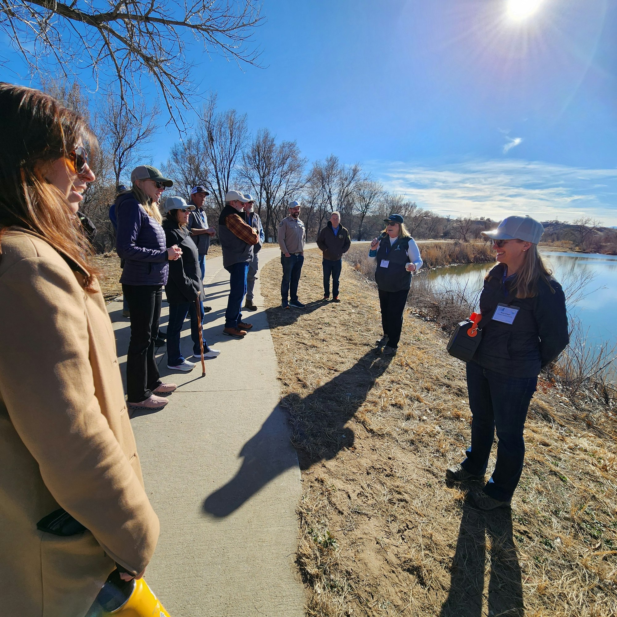 A group of people standing on a pathway outdoors, some wearing hats, in sunny weather.