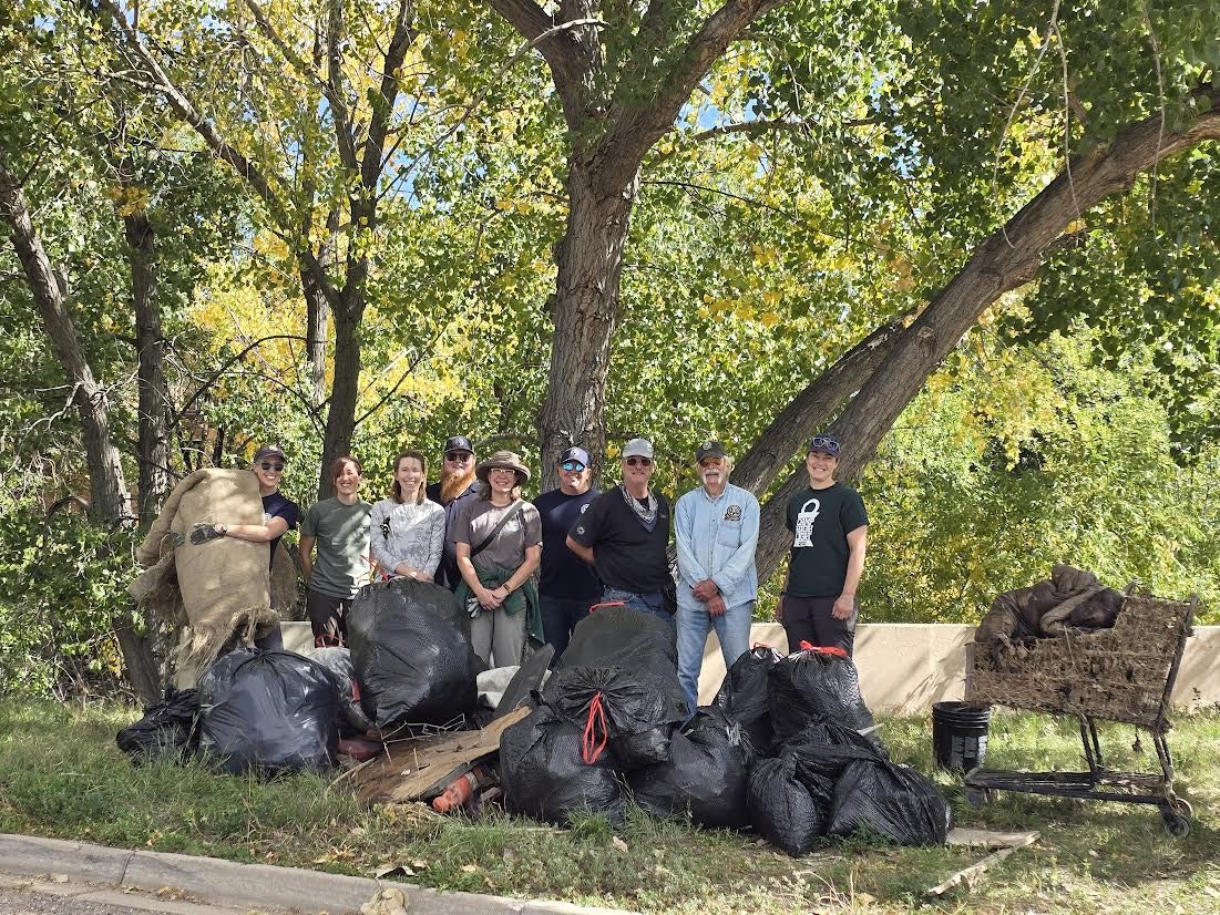 A group of people stands with bags of collected trash in a natural setting, promoting environmental cleanup and community effort.