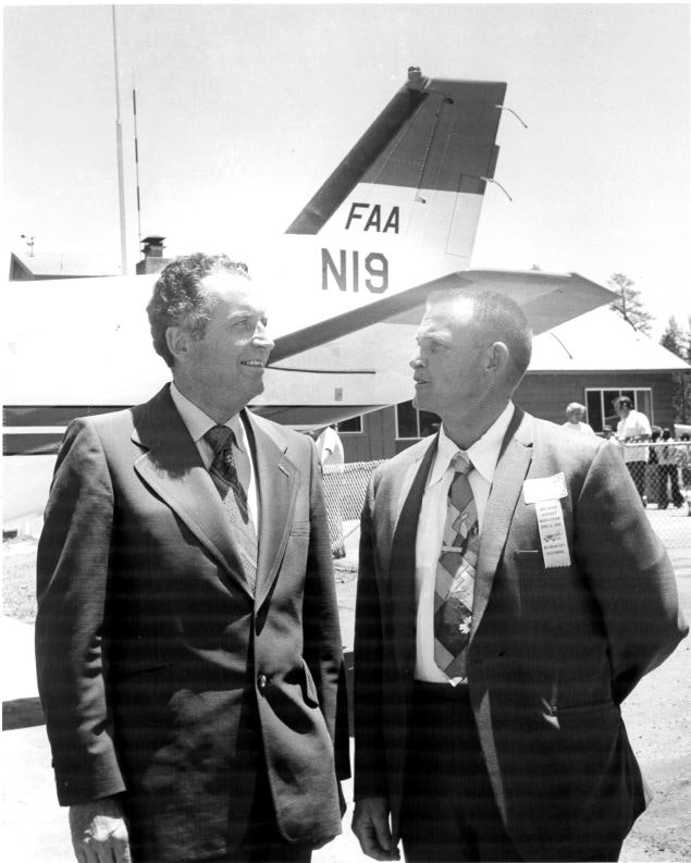 Two men in suits, standing in front of an aircraft with the tail number "N19" and "FAA" markings.